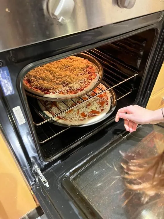 Pizza assando dentro do forno comum de fogão, vista pela porta de vidro